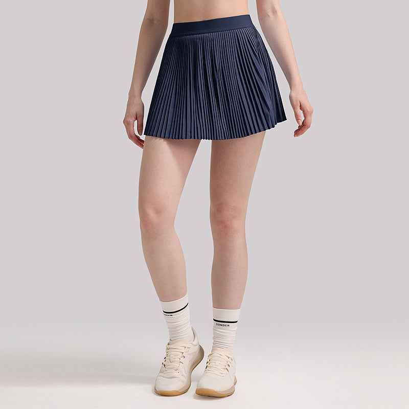 Navy Agile Pleated Lightweight Tennis Skirt with Built-In & Safety Shorts, styled with sneakers for a dynamic and sporty look.